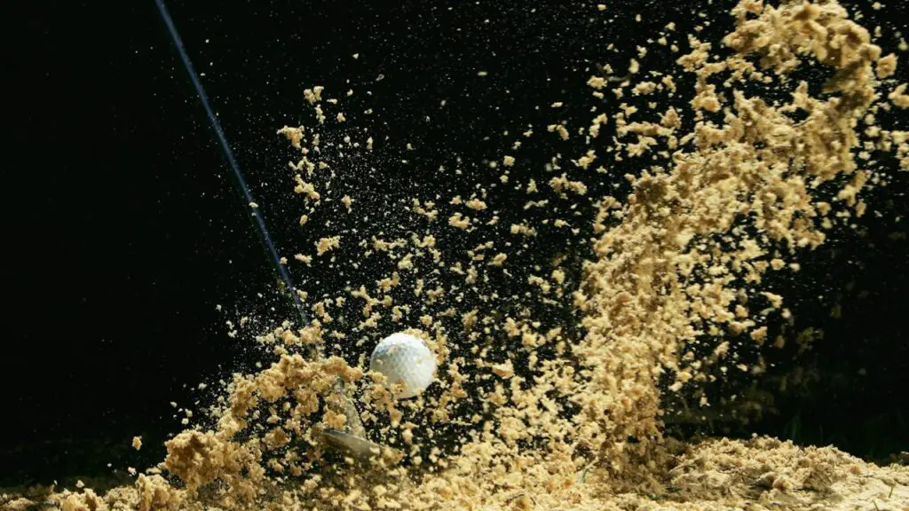 Golf ball hit in bunker with sand flying all over