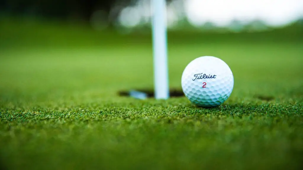Golf ball sitting near hole on golf course