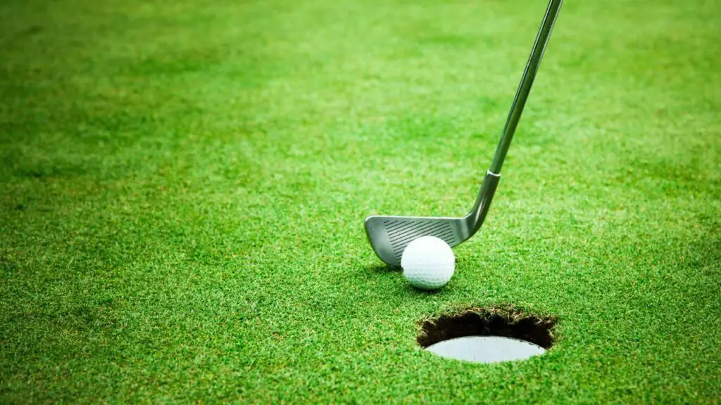 Golf club hitting golf ball into hole
