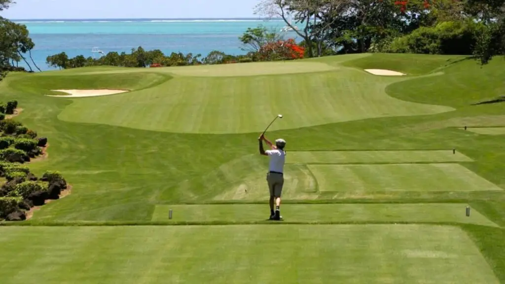 Golfer hitting golf ball on green with a scenic view of the ocean