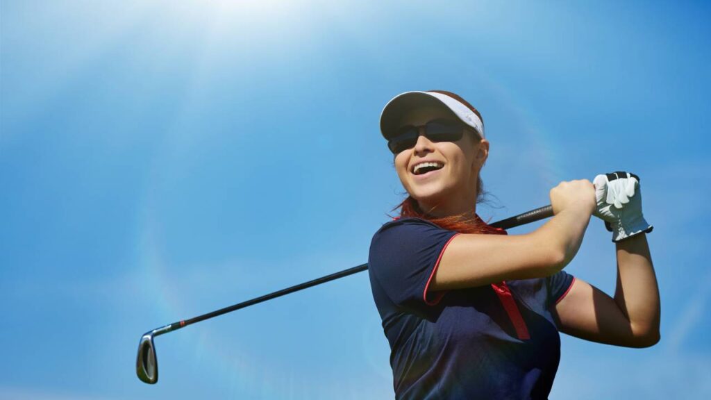 Golfer swinging golf club with blue skies and sun
