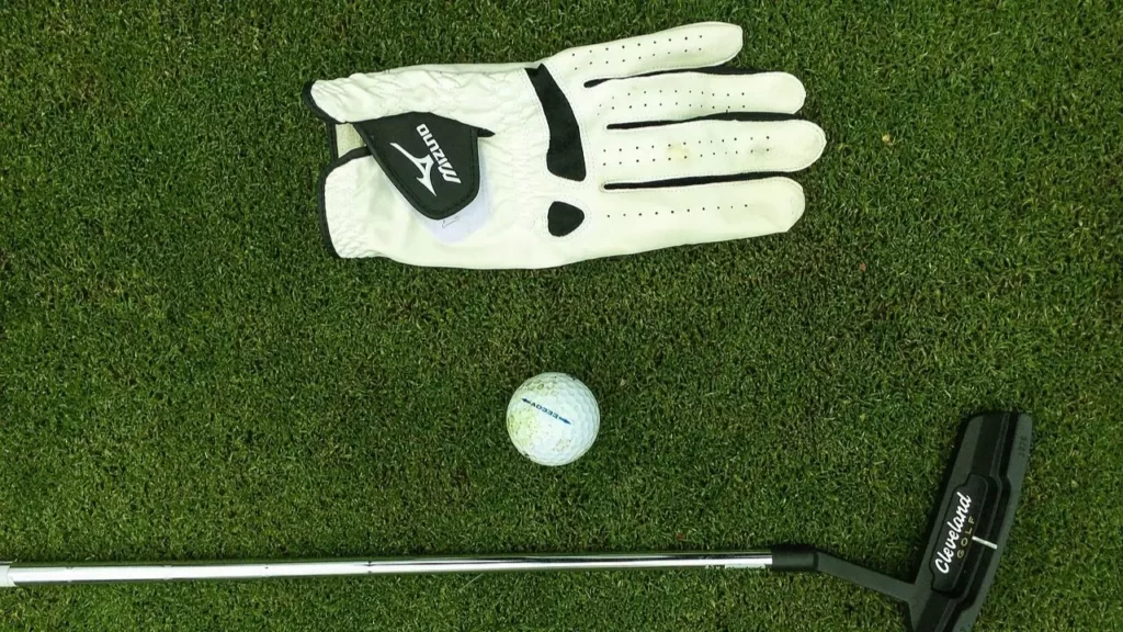 Golf glove, ball and golf wedge sitting on golf green