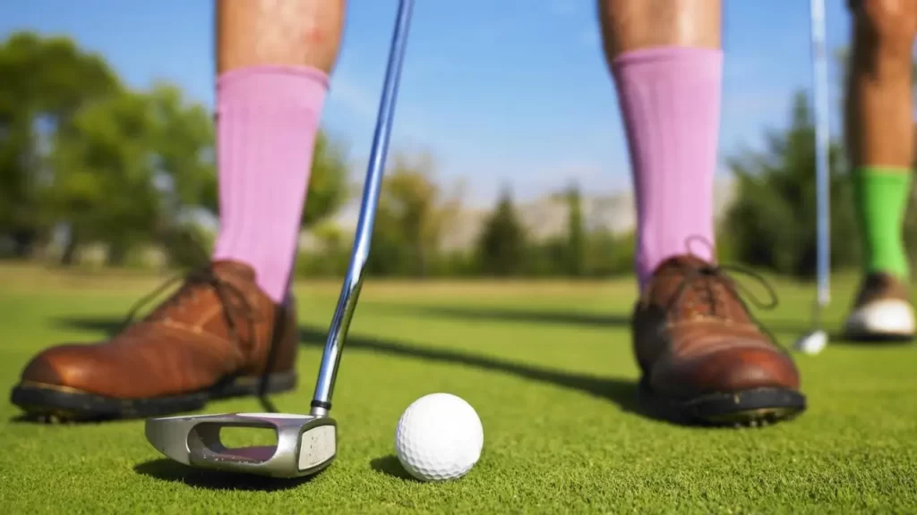 Brown golf shoes, pink socks and putter with ball