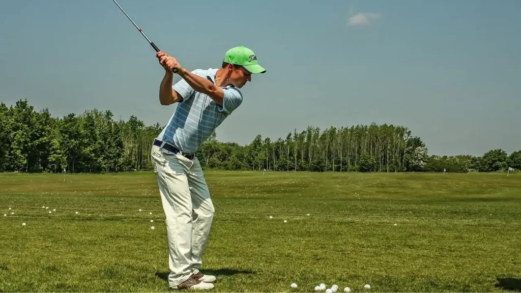 Golfer on driving range hitting golf balls wearing white pants
