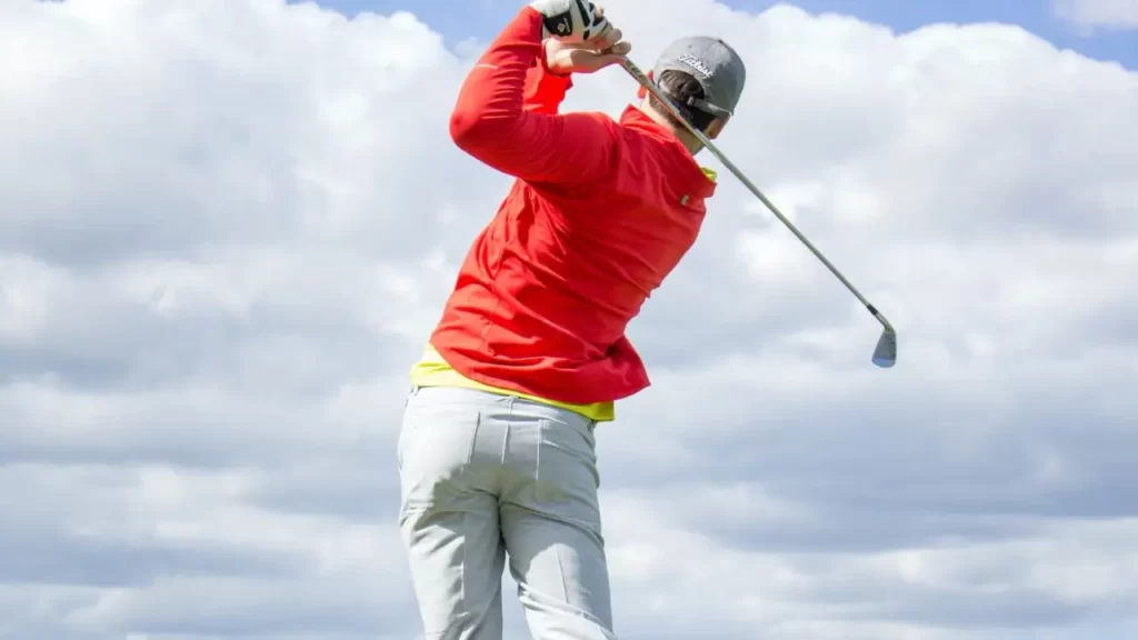 Golfer wearing white pants hitting golf shot from tee
