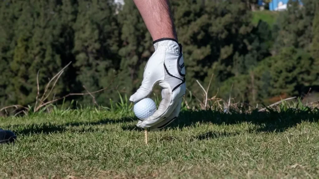 Golfer placing golf ball on golf tee wearing a golf glove