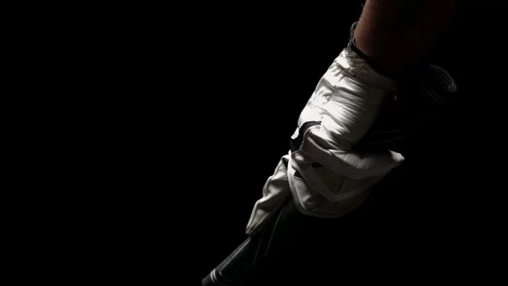 Golfer in dark room holding golf club with golf glove on