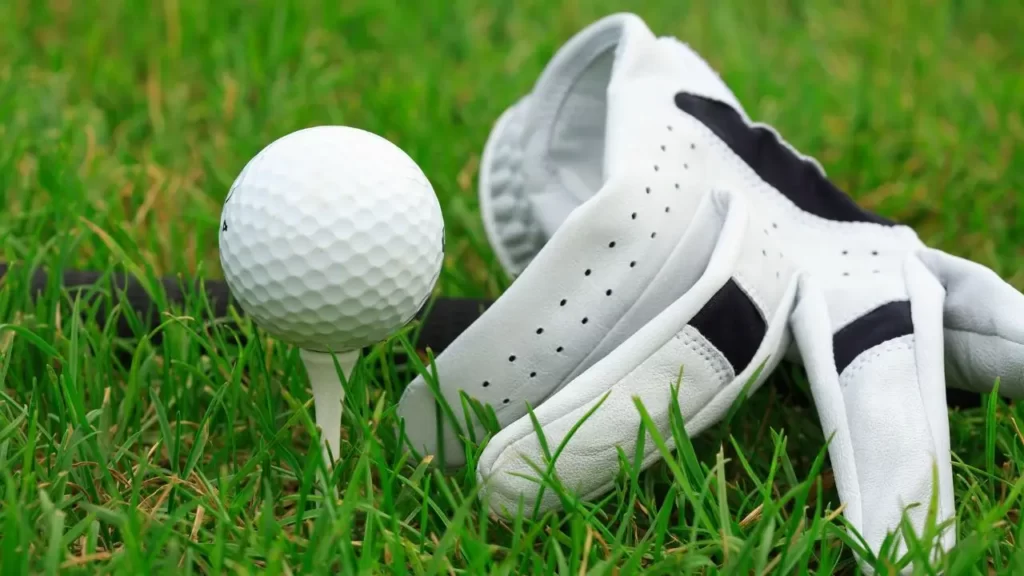 Golf Glove sitting on green grass next to golf ball and tee