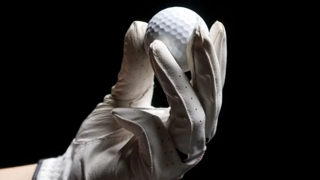 Golfer holding up golf ball with black background wearing a regular golf glove