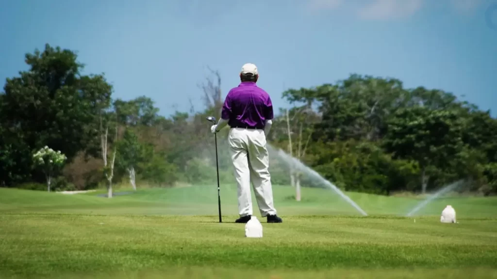 Golfer looking at water sprinklers wet golf green