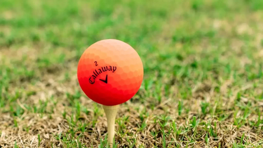 An orange golf ball sitting on a golf tee on green grass