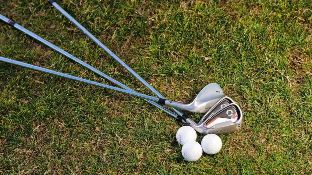 Three golf irons with three white golf balls laying on the golf grass