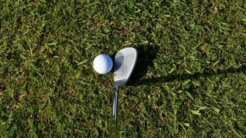 Golf wedge with golf ball on green grass with sun shining on it