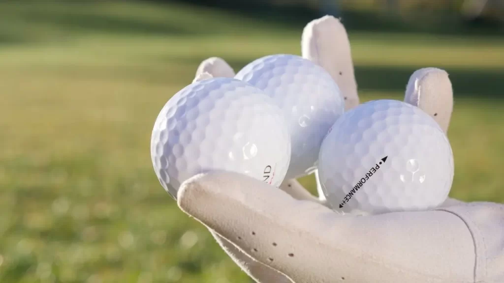 A golfer holding three golf balls in their gloved hand