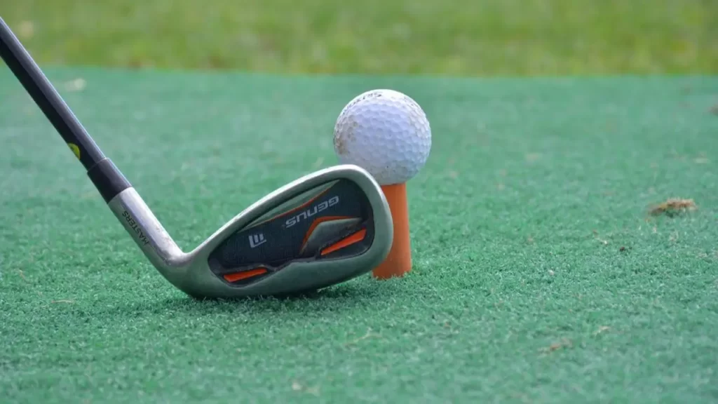 A golf ball on a orange golf tee about to be hit by a golf iron