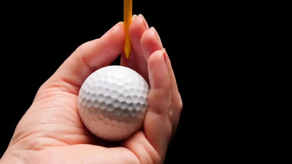A golfer holding a white golf ball and a golden golf tee in their hand