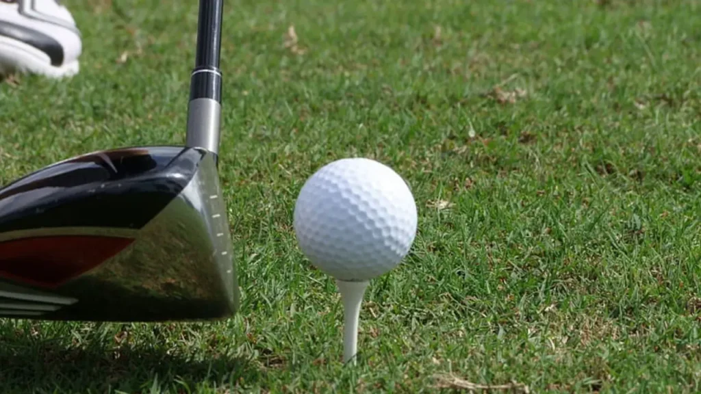 A golf ball on a golf tee on a golf course about to be hit by a golf club