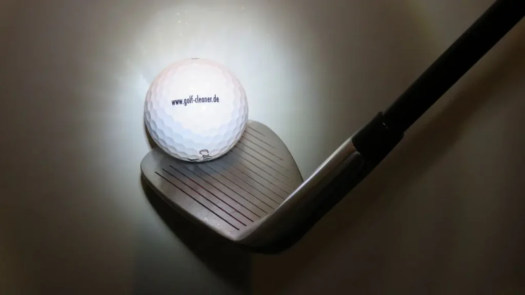 A golf ball and golf club wedge on a white background