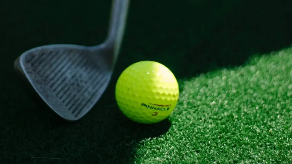 A neon yellow golf ball next to a wedge golf club