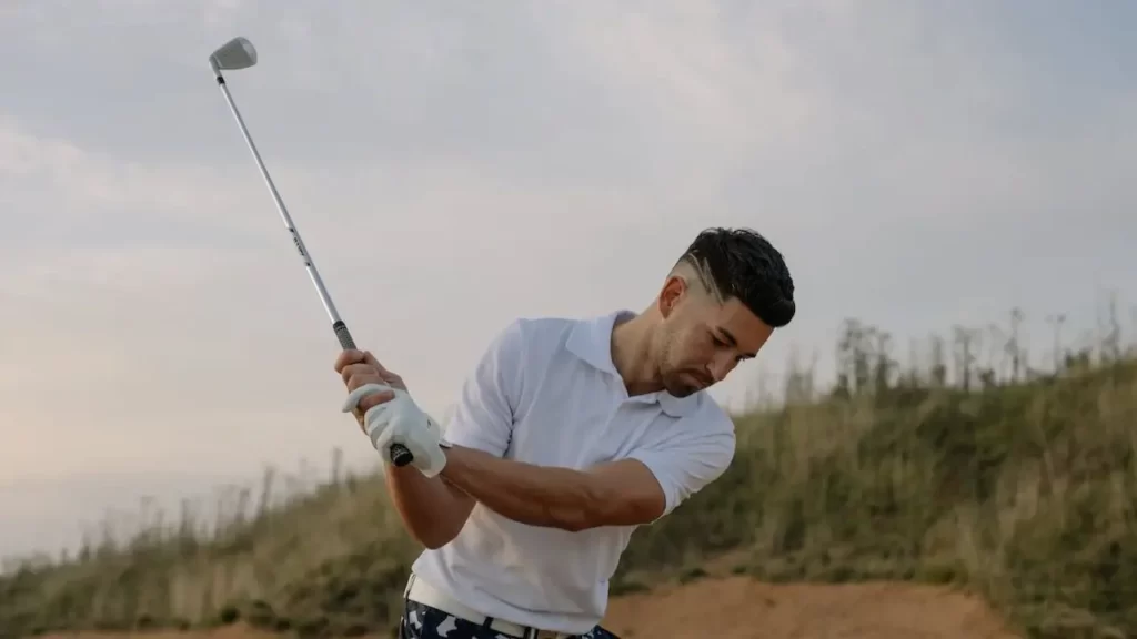 A golfer holding a golf club up as he is about to hit a golf ball