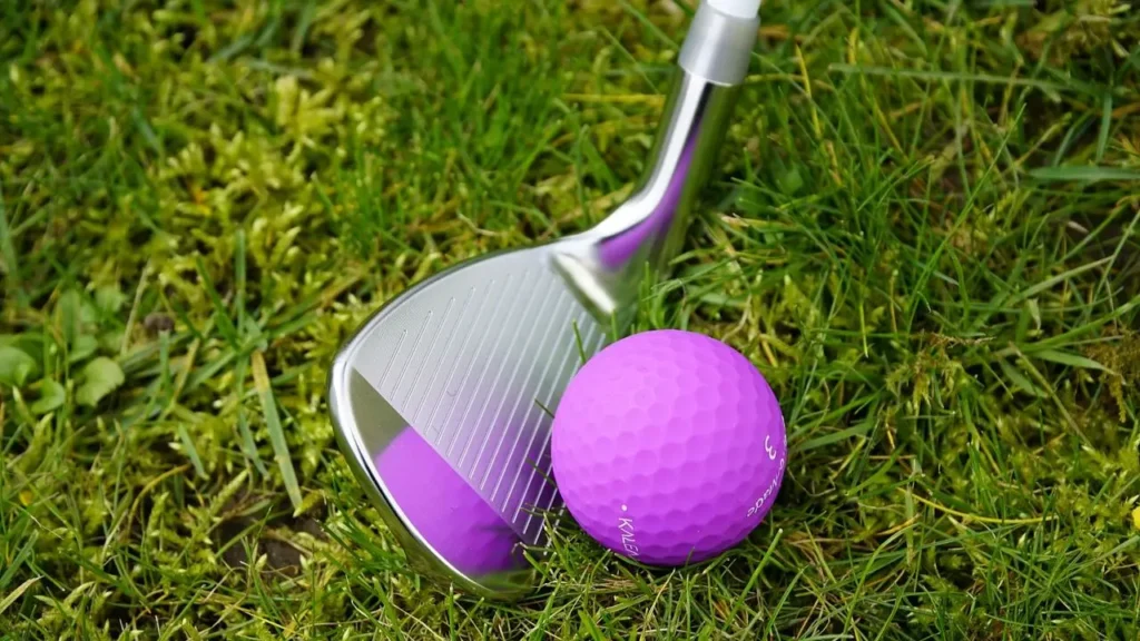 A purple golf ball being hit by a 50 degree wedge on a golf course green