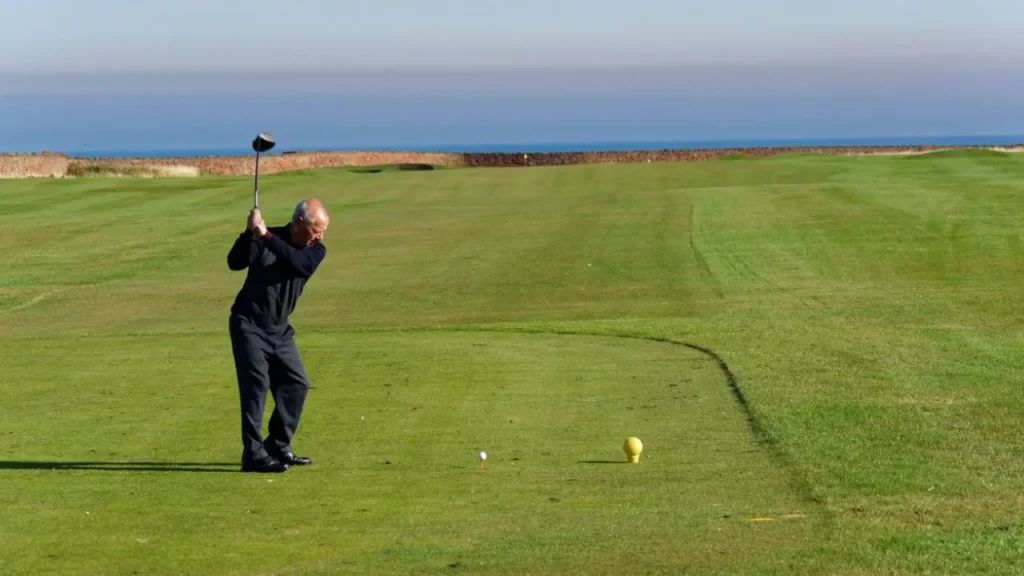 A golfer hitting a golf ball with a golf club driver on a golf course with a sea view