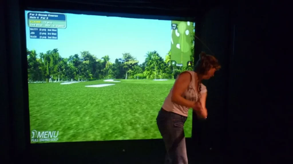 Female golfer swinging at a golf simulator screen