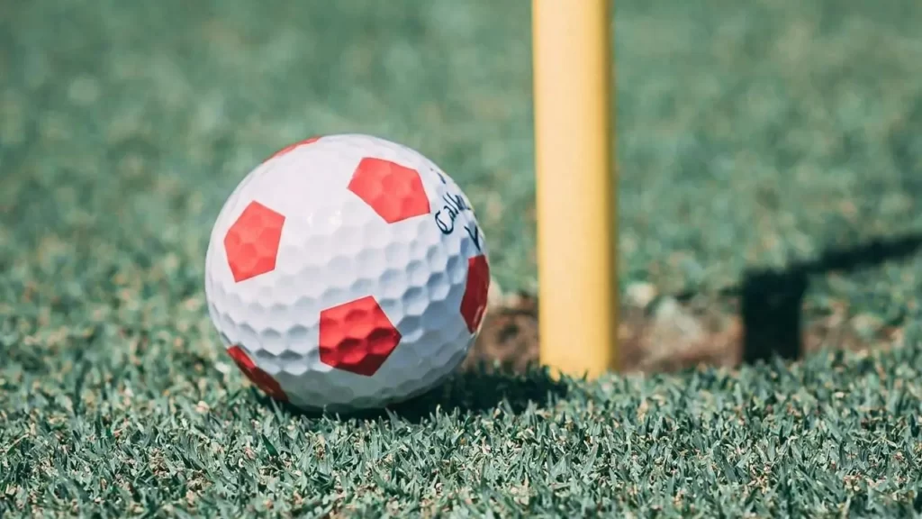 A golf ball looking like a soccer ball next to a golf course hole