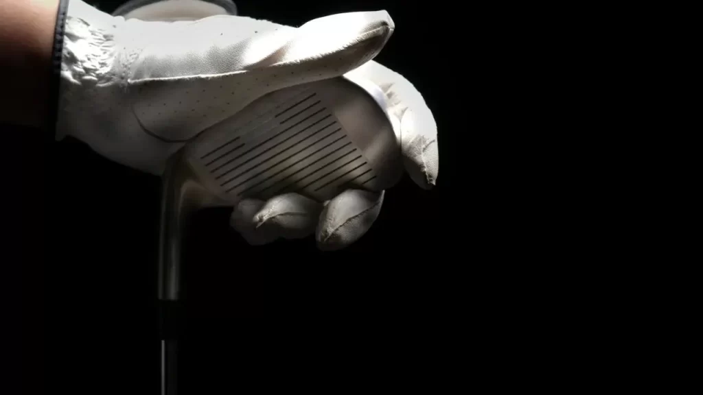 A golfer holding the base of a golf clubhead in front of a black background