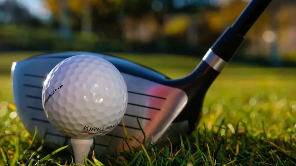 A golf club iron sitting on green grass hitting a golf ball