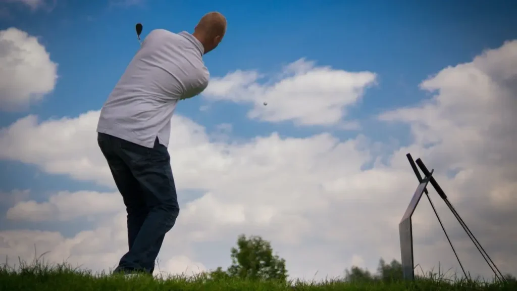 A golfer hitting a golf ball with a view from behind