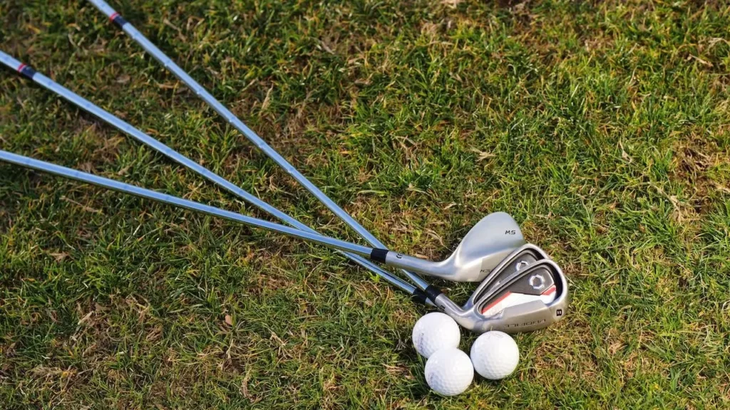 Three golf clubs lying on the green grass of a golf course with three golf balls