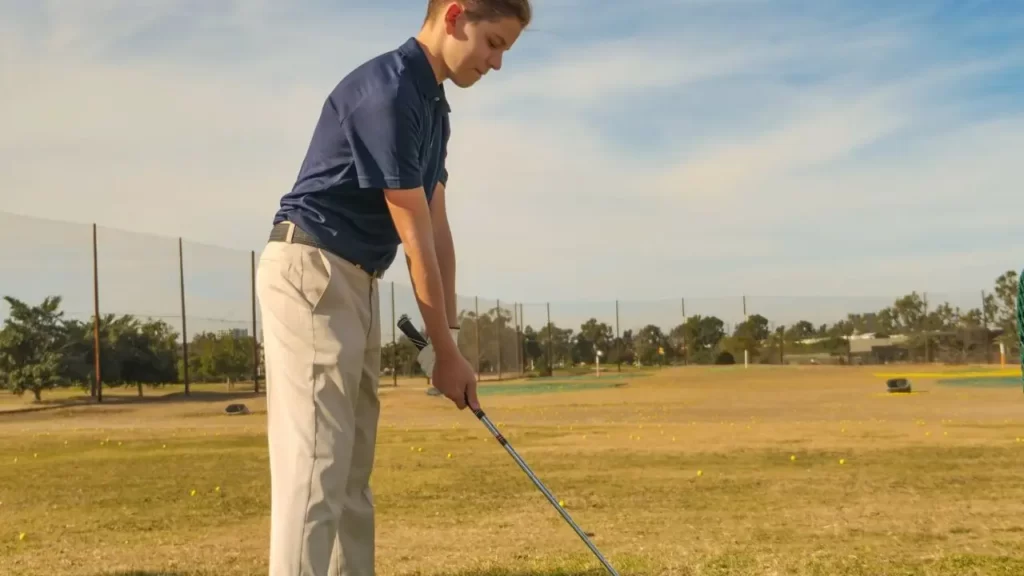 A teenage golfer holding a golf club right handed ready to tee off