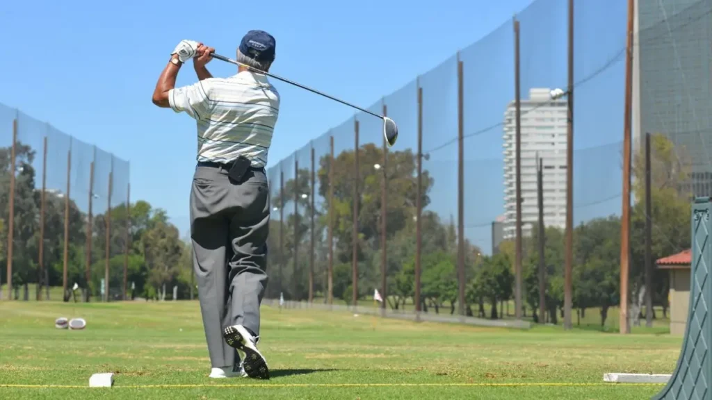 A golfer swinging a golf club on a golf course wearing a cap