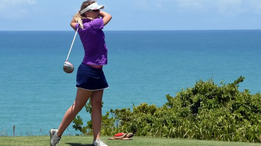 A female golfer hits a golf ball on a links golf course.