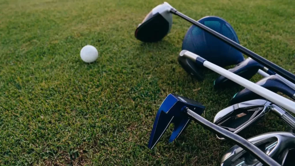 Golf clubs laying on the green grass next to a golf ball
