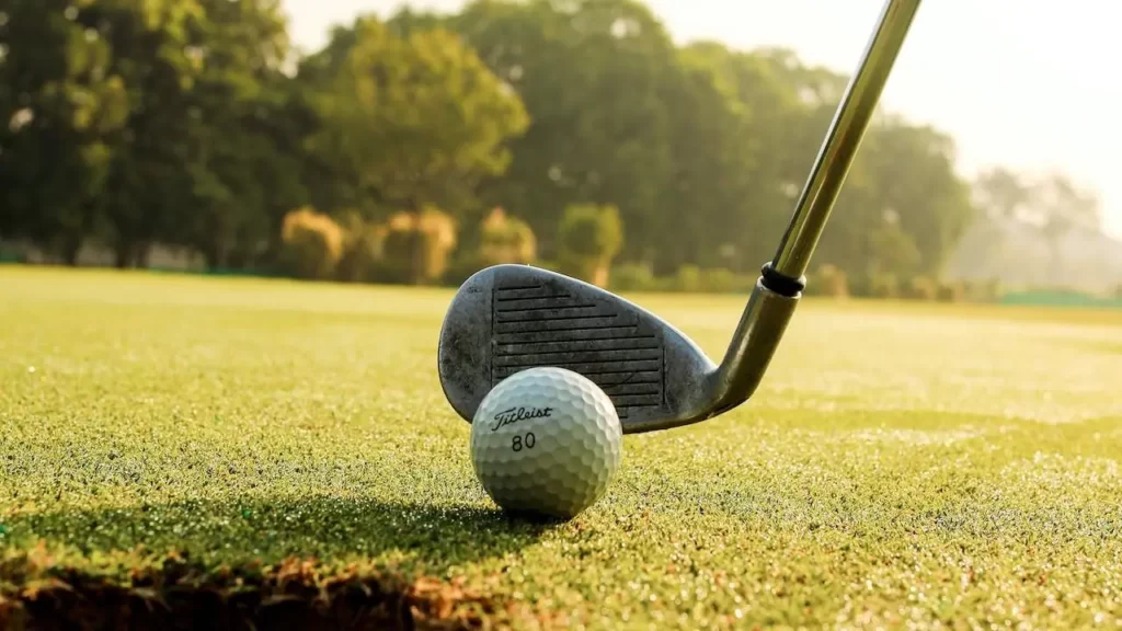 A golf wedge club lining up a shot behind a golf ball on a golf course