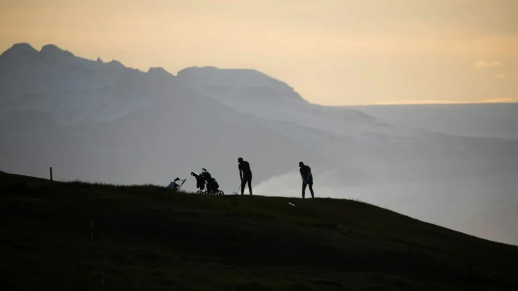 Two golfers playing golf shots on top of a mountain view of a golf course at dusk