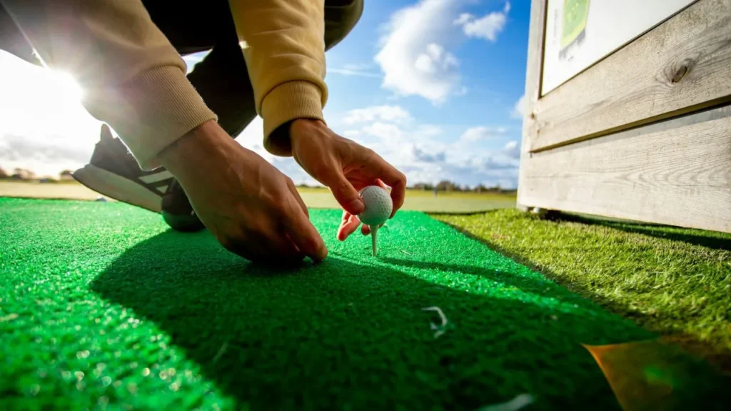A golfer setting down a golf tee on a hitting mat on a golf driving range
