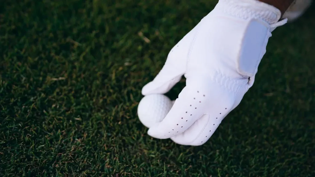 A white golf glove putting down a white golf ball