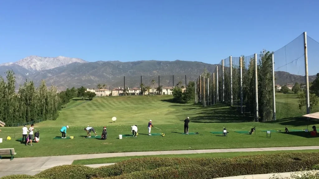 A scenic view of a green golf course with a mountain in the background where golfers are practicing on a golf driving range
